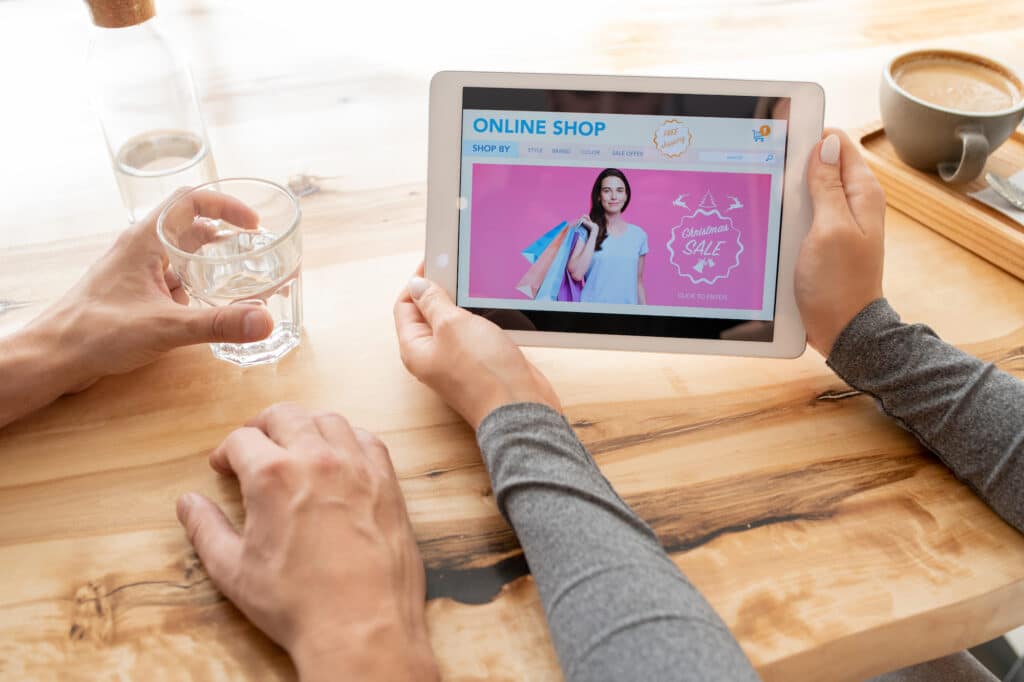 Online shopping on a tablet with Christmas sale ad. Woman holding water.